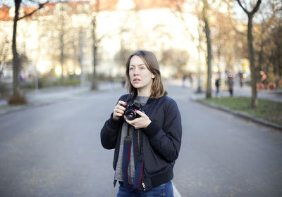 Portrait of young woman using phone while standing on tree