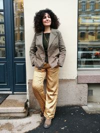 Mature woman with hands in pockets looking away while standing against wall