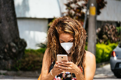 Young woman looking at mobile phone with an ffp2 mask