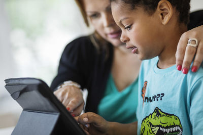 Mother assisting son in using digital tablet at home