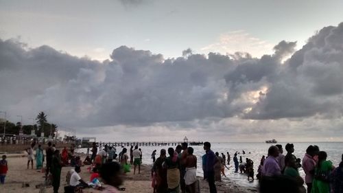 People on beach against cloudy sky