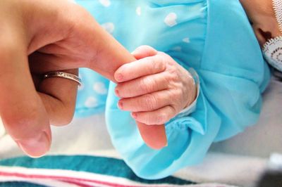 Close-up of newborn baby girl holding mother finger in hospital