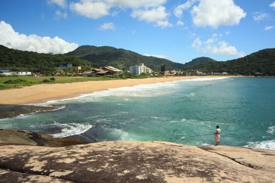 Mid distance of man fishing in sea while standing on rock against sky