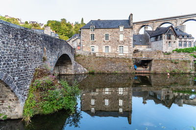 Arch bridge over canal by old building against sky