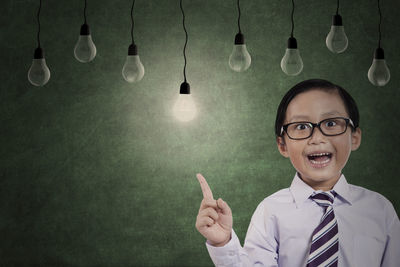 Portrait of boy looking at light bulbs while standing against wall