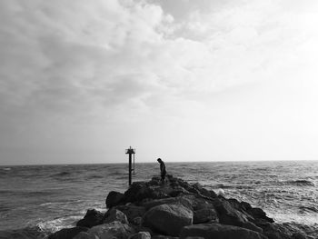 Man standing on rocks by sea against sky