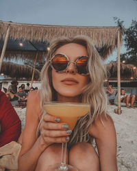 Portrait of woman holding sunglasses against sky