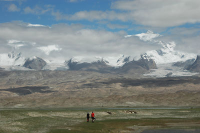 Rear view of hikers walking on field by snowcapped mountains against sky