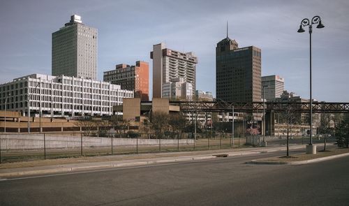 Road by buildings against sky in city