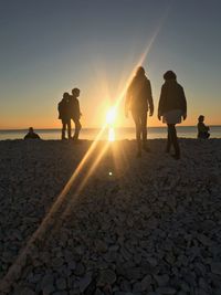 Silhouette people walking at beach against sky during sunset