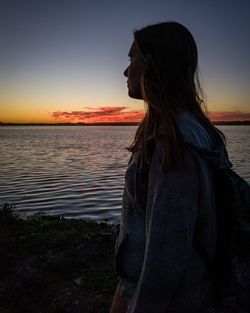 Woman standing at beach against clear sky during sunset