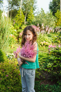 Portrait of girl holding flowers against trees