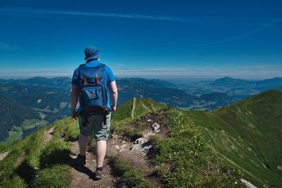 Rear view of hiker looking at mountains against blue sky