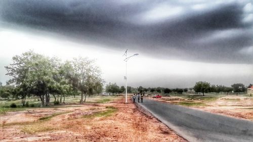 Road passing through field against cloudy sky