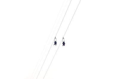 Low angle view of people zip lining against clear sky