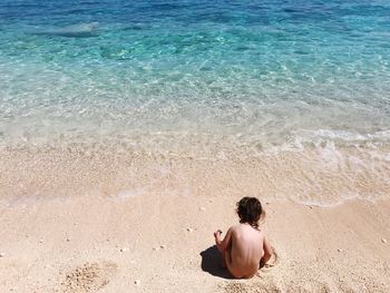 High angle view of naked girl crouching on shore at beach