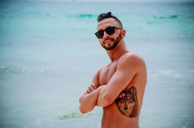 Portrait of shirtless man wearing sunglasses while standing at beach