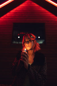 Portrait of woman holding red while standing against illuminated building