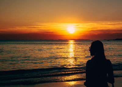 Rear view of woman standing on beach during sunset