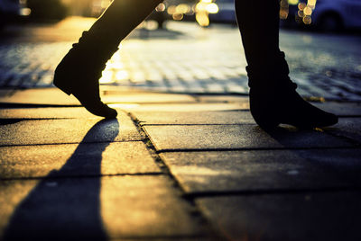 Low section of woman walking on street during sunset