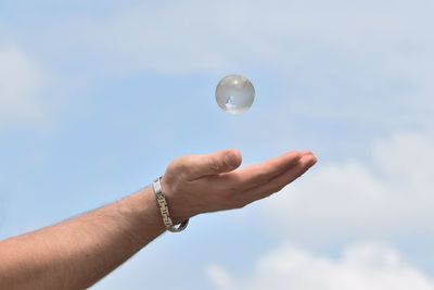 Cropped hand with crystal ball in mid-air against sky