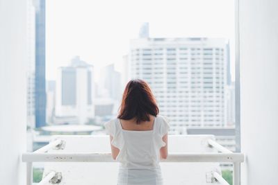 Rear view of woman standing by window in city