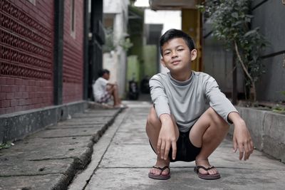 Portrait of smiling boy crouching on footpath