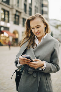 Smiling entrepreneur using smart phone while standing in city