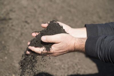 Cropped hands of man pouring soil outdoors