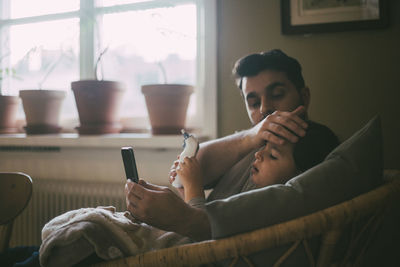 Father checking temperature of son while sitting in living room at home