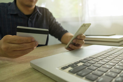 Midsection of man holding credit card while using mobile phone