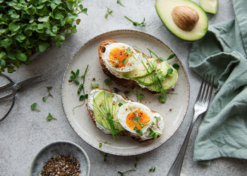 Bread toast, boiled eggs, avocado slice, microgreens on a plate, breakfast time