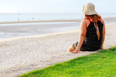 Rear view of woman wearing hat sitting at beach