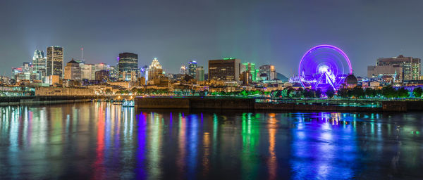 Illuminated city by river against sky at night