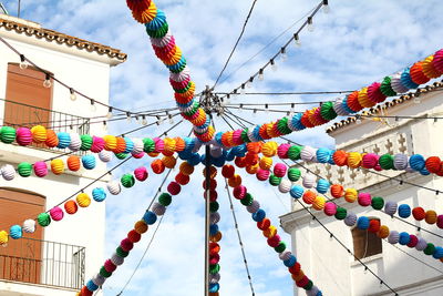 Low angle view of multi colored umbrellas hanging amidst buildings against sky