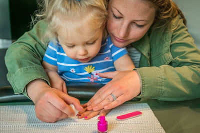 Mother painting fingernail of cute daughter at home