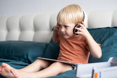 Cute boy using digital tablet while sitting on bed at home