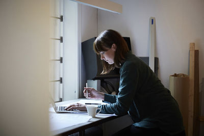 Side view of confident female architect using laptop in office