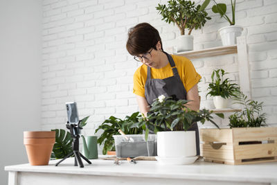 Side view of woman holding potted plant at home