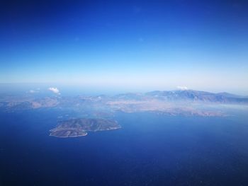 Aerial view of sea and mountains against blue sky