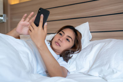 Woman using mobile phone while lying down on bed at home