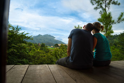 Rear view of couple sitting on boardwalk against sky