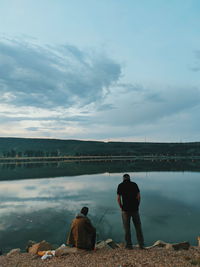 Rear view of men standing by lake against sky