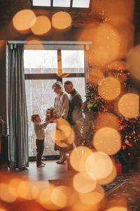 Portrait of happy family in knitted beige sweaters waiting santa indoor.