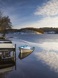 The morning sun reflects off the calm lake, framed by a jetty and snow-covered trees. 