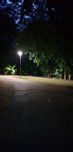 Empty road amidst trees against sky at night