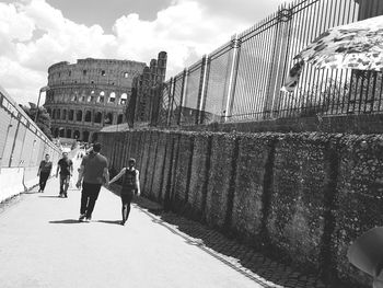 People walking in city against cloudy sky