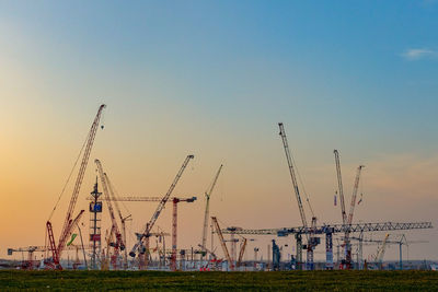 Cranes at construction site against sky during sunset