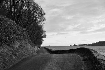 Scenic view of road along sea against cloudy sky