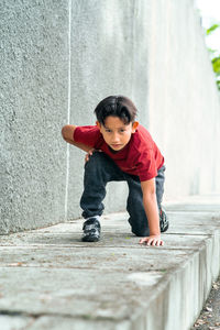 Full length portrait of boy kneeling on footpath